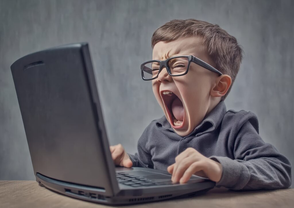 Enfant portant des lunettes criant devant un ordinateur portable, expression de stress et de frustration.